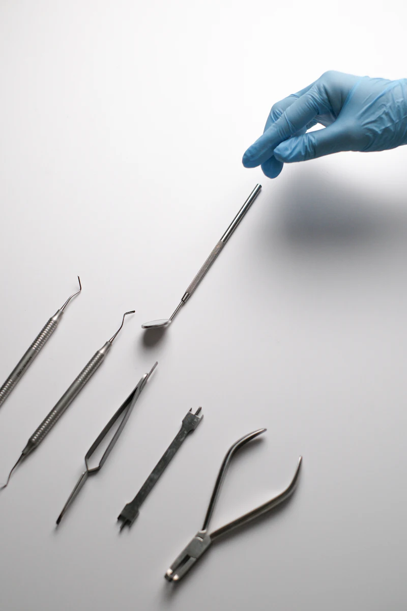 A gloved finger pointing at fine dental instruments laid out on a white tray