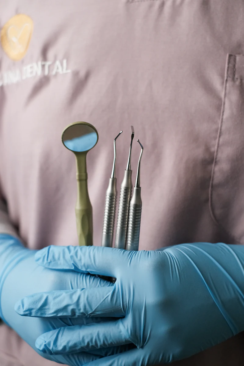 A gloved hand holding a dental mirror and fine dental instruments